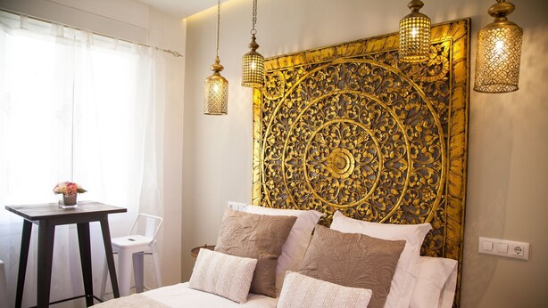 A bedroom with a large bed, two bedside tables, a small table with a vase of flowers, and a chair. - Suites Miguel Ángel - Adults Only (Madrid)