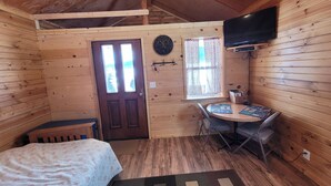 Una habitación de cabaña acogedora con cama, una mesita con sillas, televisor y ventana con cortinas.