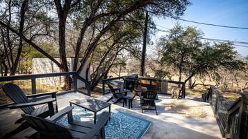 A patio with Adirondack chairs, a table, and a grill.