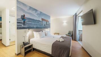 Una habitación de hotel moderna con una cama grande, un televisor de pantalla plana, un escritorio con teléfono y un cuadro de una persona excursionando.