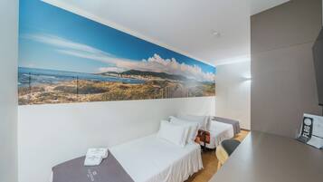 A hotel room with two beds, a large beach mural on the wall, and a desk with a flag.