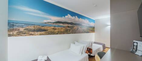 Habitación de hotel con dos camas, un gran mural de playa en la pared y un escritorio con una bandera.