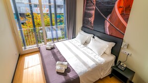 A hotel room with a large bed, a view of a balcony with plants, a painting on the wall, and a telephone on the nightstand. - Flag Design Hotel (Viana do Castelo)