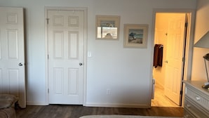 A bedroom with a bed, a dresser, and two doors. There are two framed pictures on the wall.