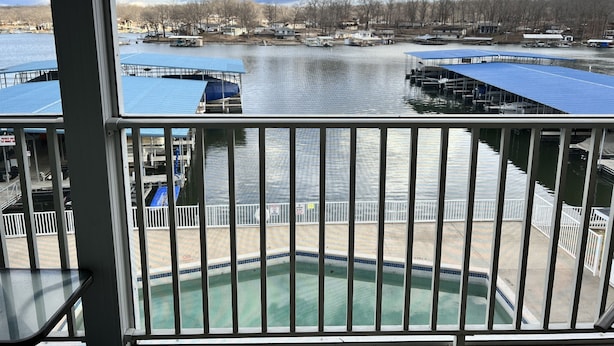 A view from a balcony overlooking a marina with boats docked, a swimming pool, and a distant shoreline with buildings.
