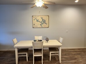 Un coin repas comprenant une table et quatre chaises, un ventilateur de plafond et une carte accrochée au mur.