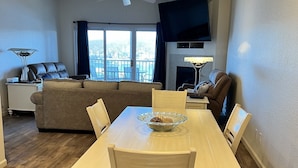 A dining area with a table and chairs, a ceiling fan, a sofa, a TV, and a view of the outdoors.