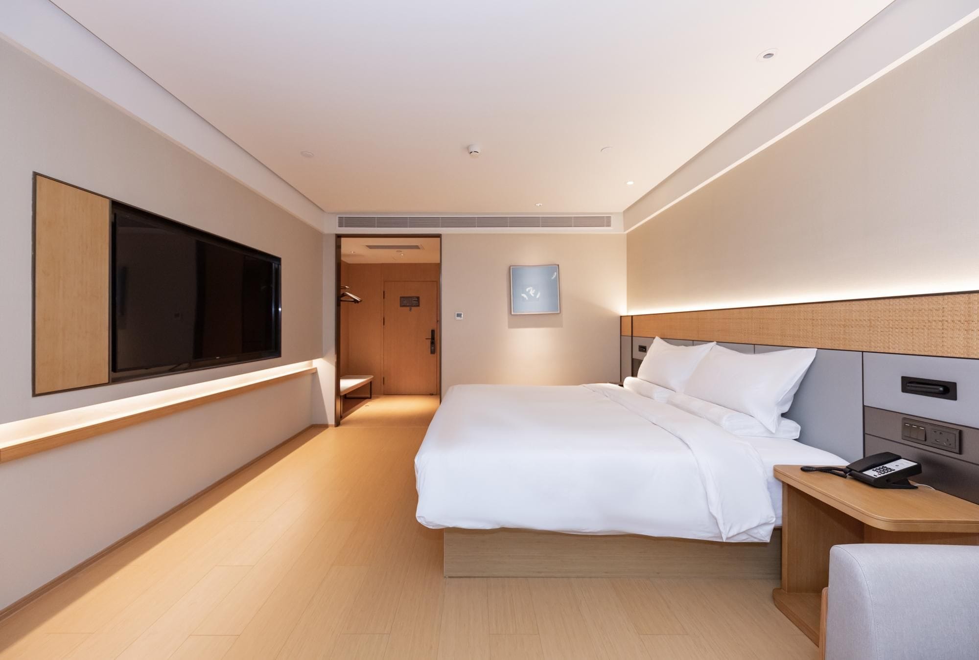 Une chambre d’hôtel avec un grand lit, une table de chevet avec un téléphone, un téléviseur fixé au mur et une porte donnant sur une salle de bain.