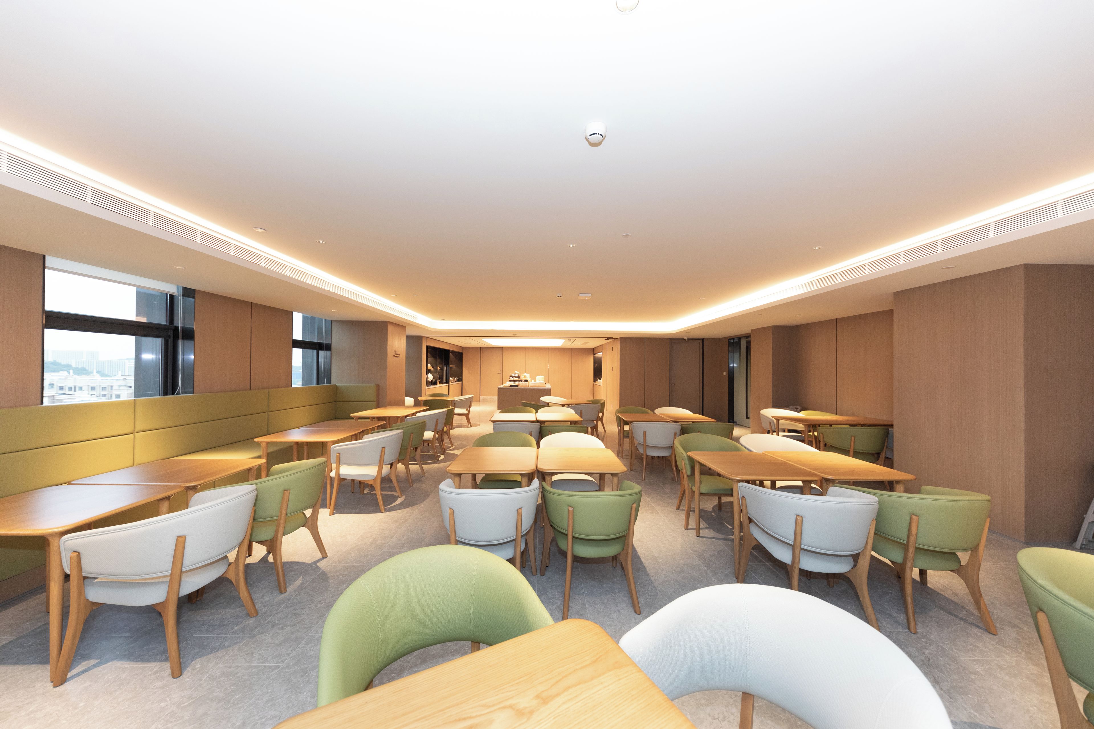 A modern dining area with multiple tables and chairs, a central counter, and large windows providing natural light.