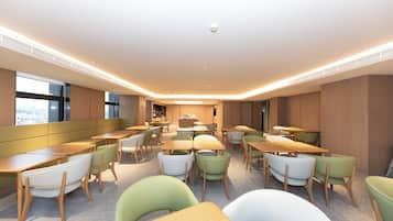 A modern dining area with multiple tables and chairs, a central counter, and large windows providing natural light.