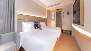 Habitación de hotel con dos camas, un sofá, un televisor y un baño visible a través de una puerta de cristal.