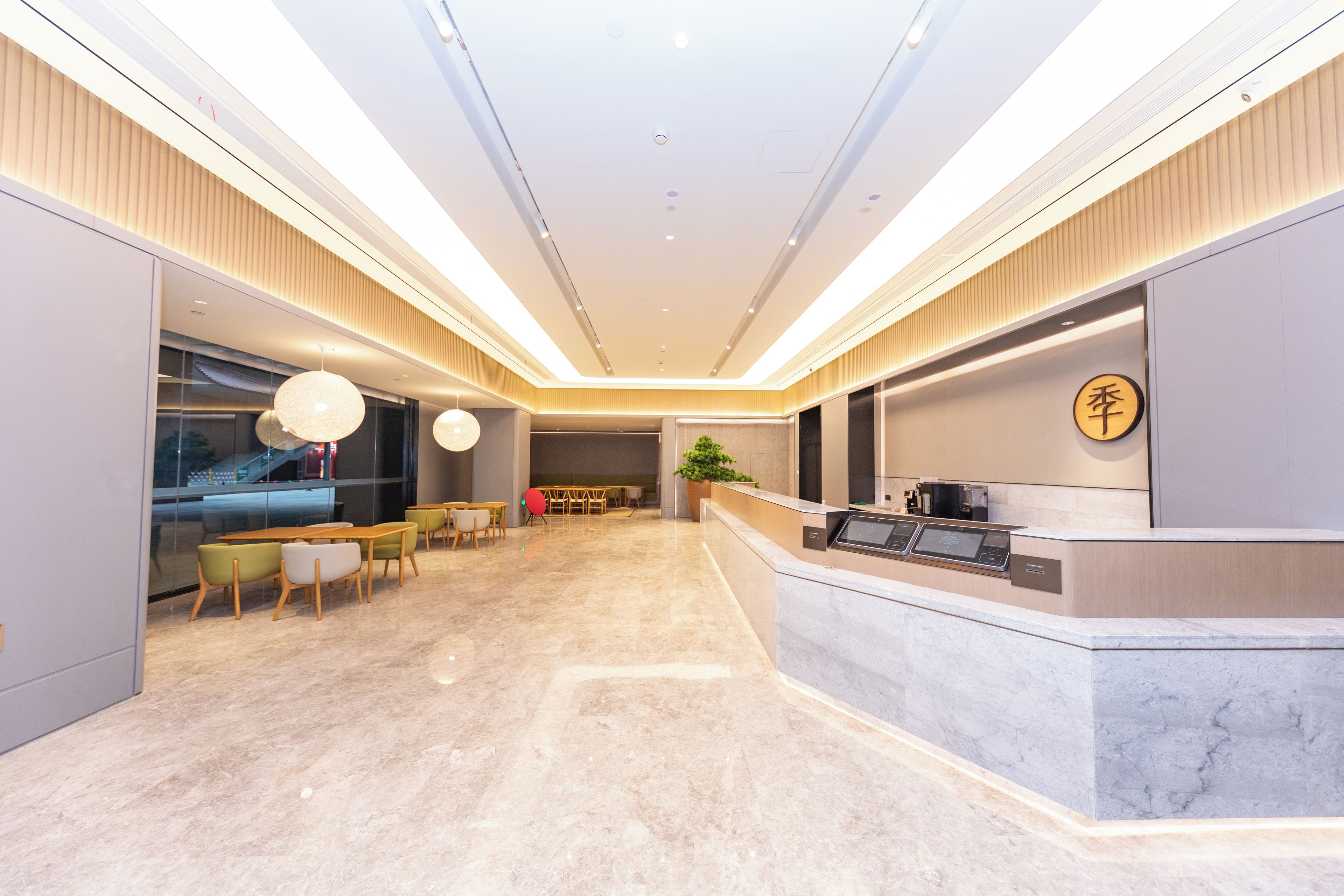 A modern hotel lobby with a reception desk, seating area, and a large window.