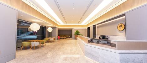 Un hall d’hôtel moderne avec un comptoir d’accueil, un espace salon et une grande fenêtre.