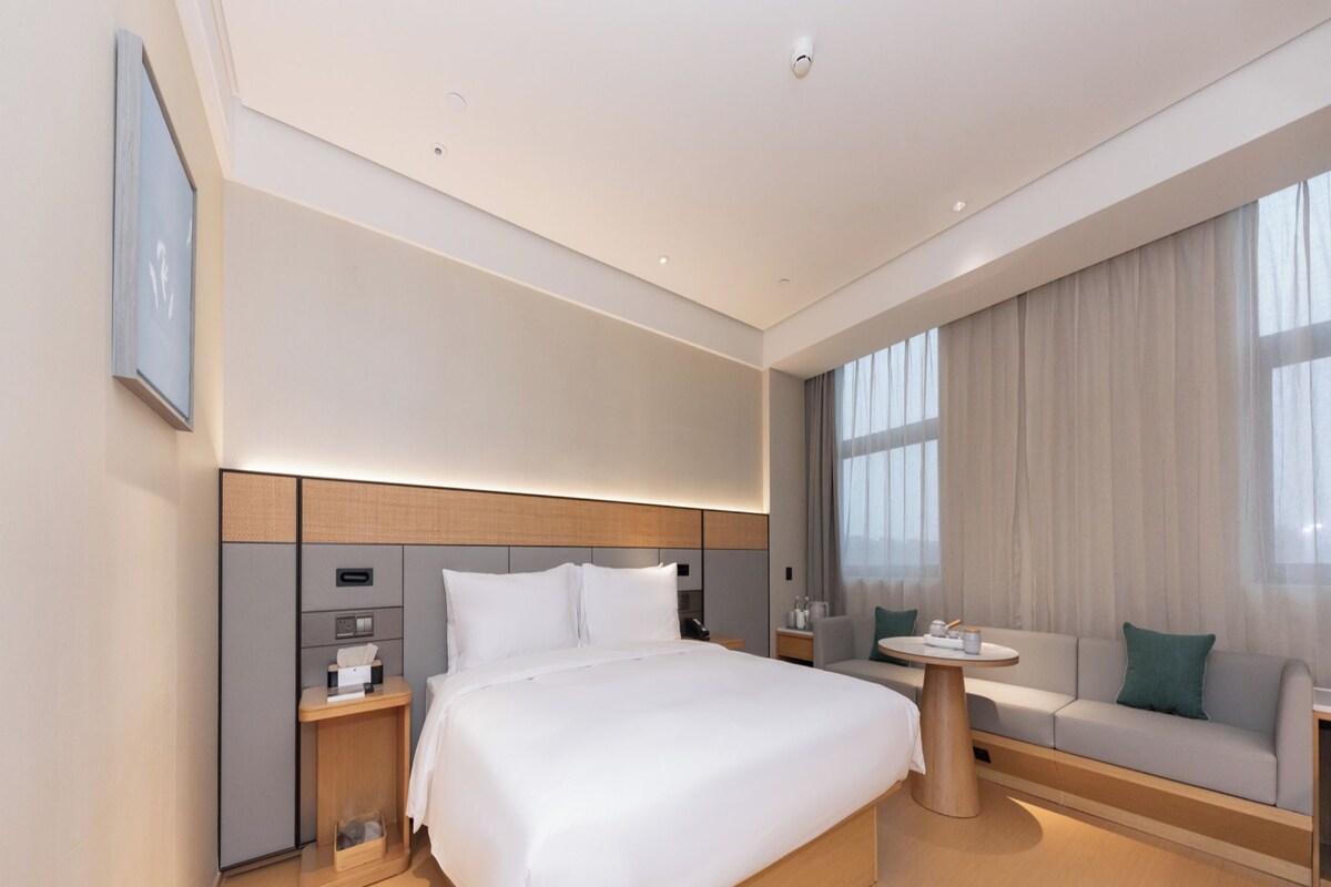 A modern hotel room with a large bed, bedside tables, a sofa, and a small table.