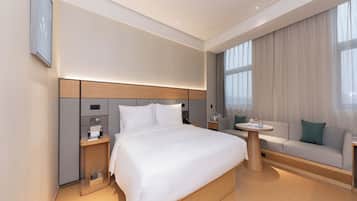 A modern hotel room with a large bed, bedside tables, a sofa, and a small table.