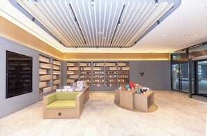 A modern library interior with bookshelves, seating areas, and a ceiling with linear light fixtures. - Ji Hotel (Nanjing)