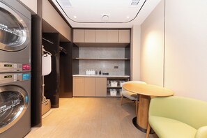A compact hotel room with a washing machine, a small kitchenette, a seating area, and a closet. - Ji Hotel (Nanjing)