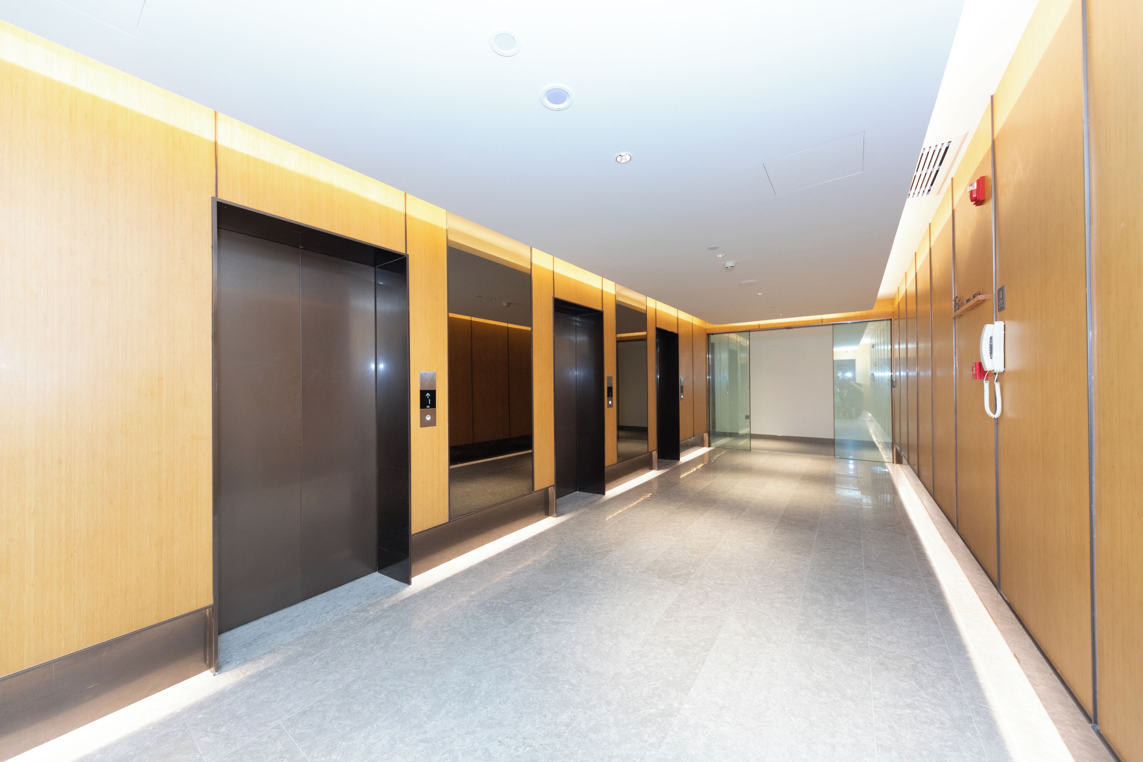 A modern hallway with elevators and a fire alarm on the wall.