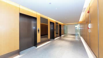 A modern hallway with elevators and a fire alarm on the wall.