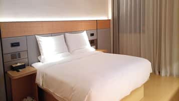 Una habitación de hotel moderna con una cama grande, cabecero de madera, mesitas de noche y un ventanal con cortinas.