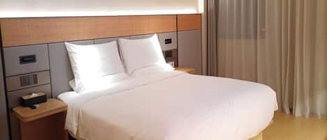 A modern hotel room with a large bed, wooden headboard, bedside tables, and a large window with curtains.