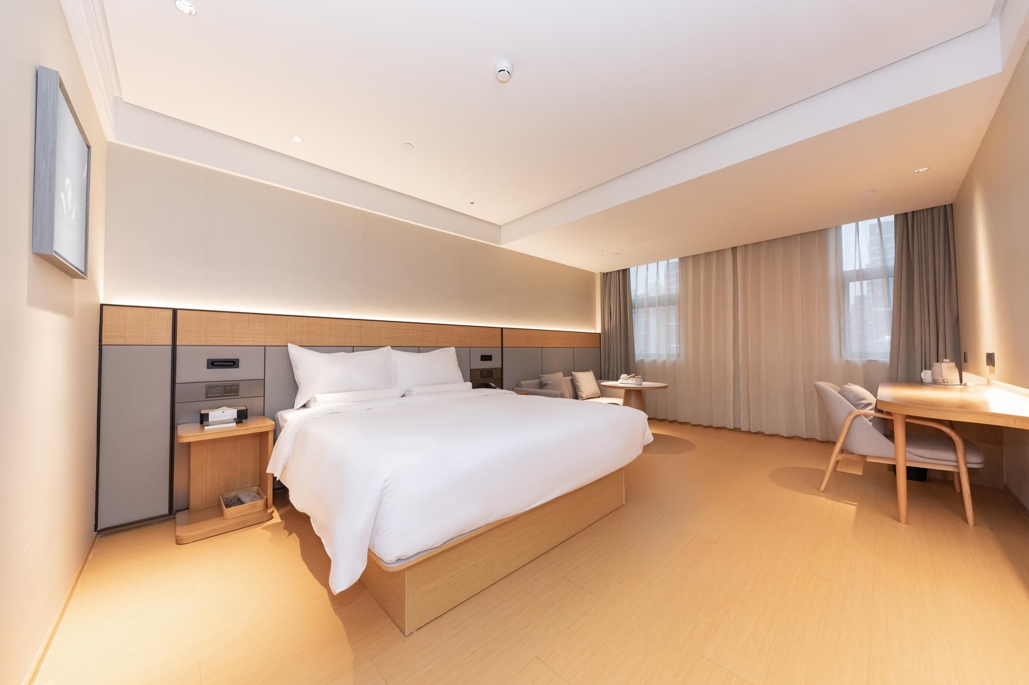 A modern hotel room with a large bed, bedside tables, a desk, and a chair.
