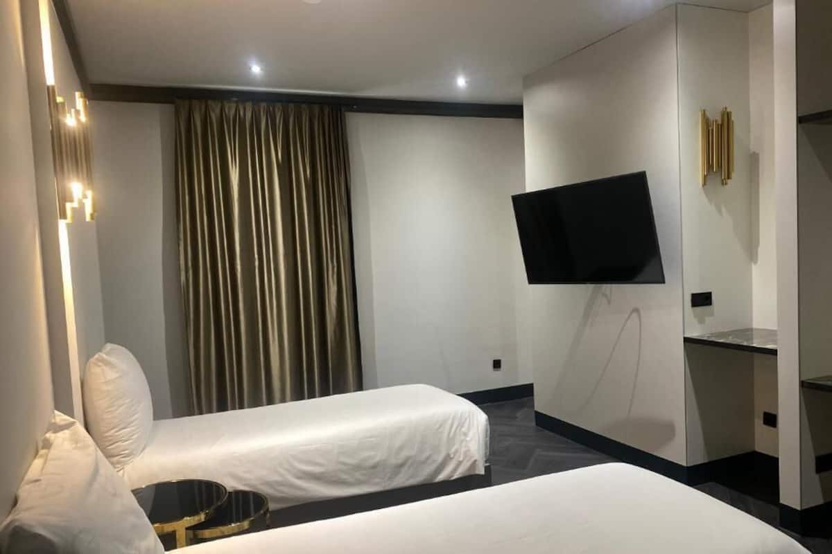 A hotel room with two beds, a flat-screen TV mounted on the wall, and a large window with curtains.