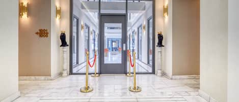 A hotel lobby with marble flooring, gold stanchions, and a glass entrance.