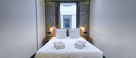 A modern hotel room with a large bed, two bedside tables with lamps, and a view of a building through a window.