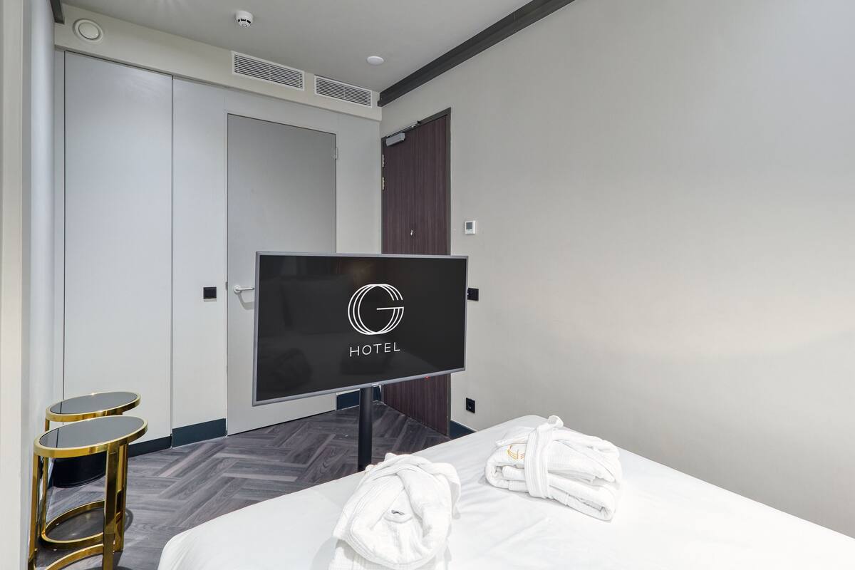 A hotel room with a bed, a TV, a wardrobe, and a small table.