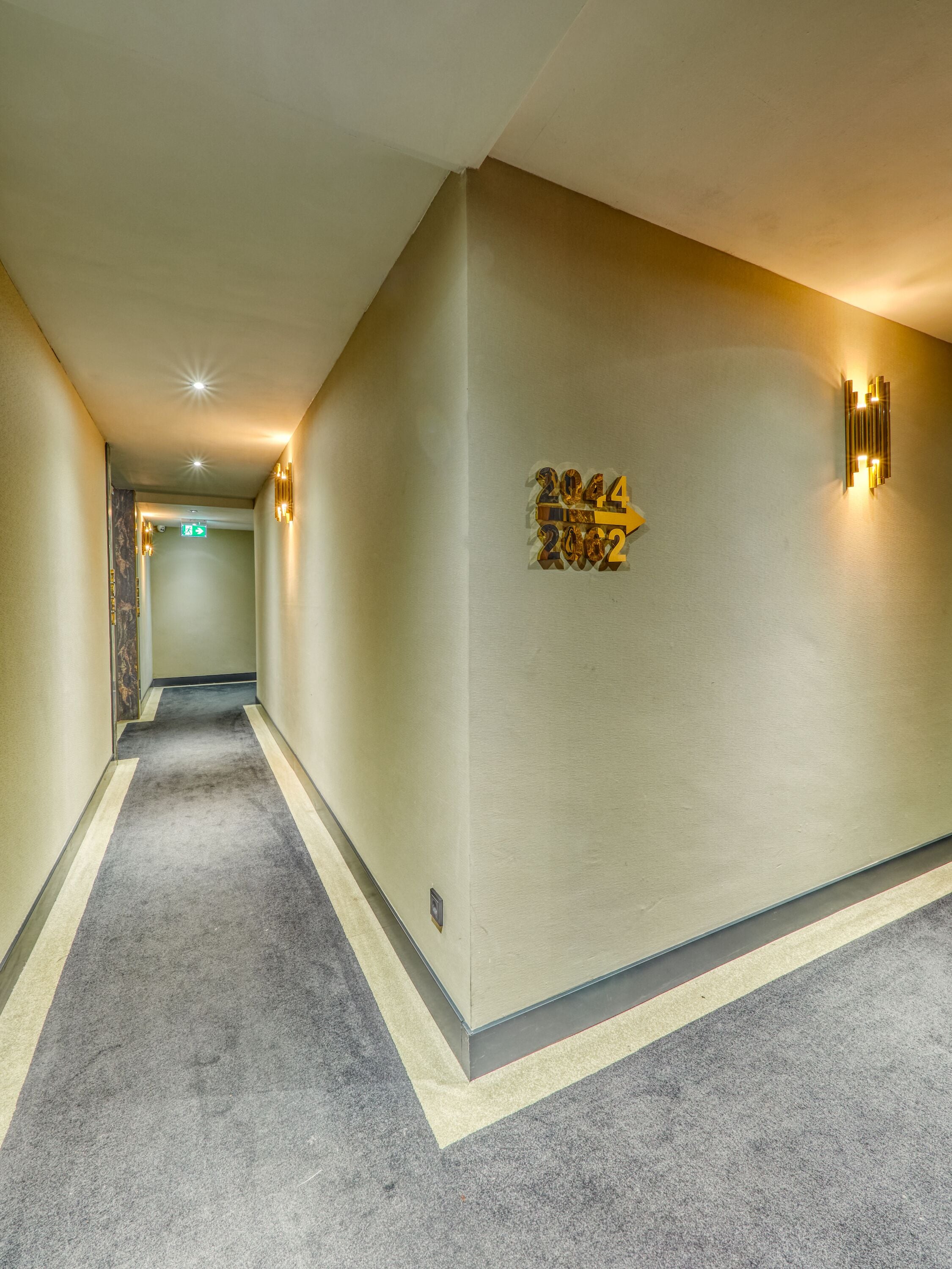 A hotel hallway with a carpeted floor, a wall-mounted sign with the year 2024, and wall sconces.