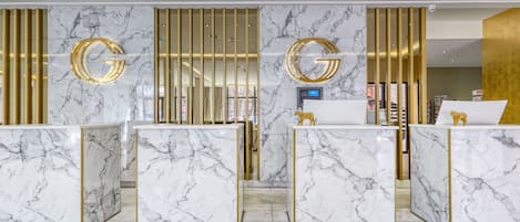 Un hall d’accueil d’hôtel avec un comptoir de réception en marbre, des éléments décoratifs dorés et un design moderne.