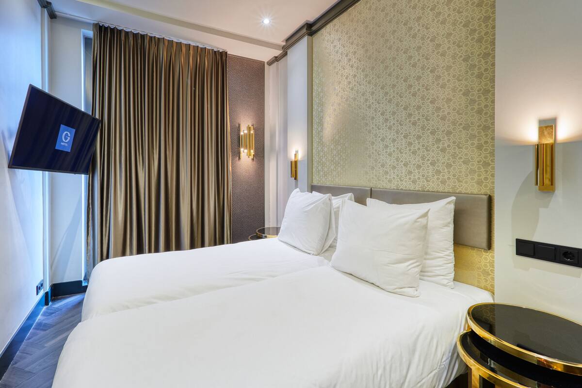 A hotel room with a large bed, a flat-screen TV mounted on the wall, and a wall-mounted light fixture.