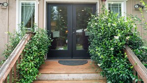 A wooden staircase leading to a black door with a doormat, flanked by lush green plants. - Large private retreat (Union)