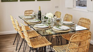 A dining room with a glass table set for six, surrounded by wicker chairs, with a bottle of champagne and white flowers on the table. - 4 bedroom accommodation in Middleton-on-Sea, near Bognor Regis (Middleton-on-Sea, near Bognor Regis)