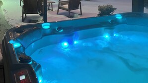 Un jacuzzi con luces LED azules, rodeado de mobiliario exterior y nieve en el suelo.