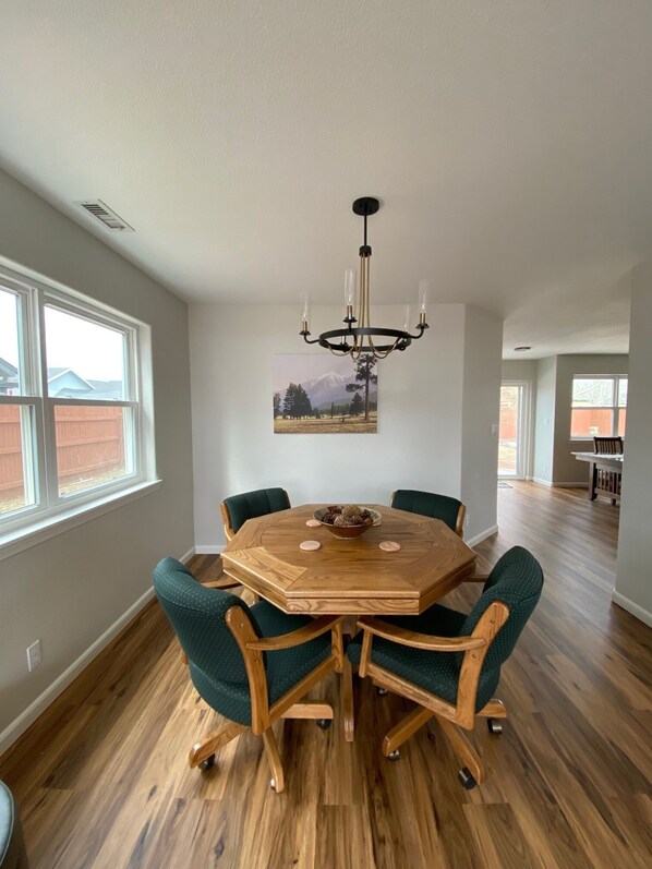 A dining area with a round wooden table, green upholstered chairs, and a chandelier.