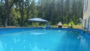A clear swimming pool with a blue tiled edge, surrounded by trees and a covered area. - Human Hotel Résidence  (Villecroze)