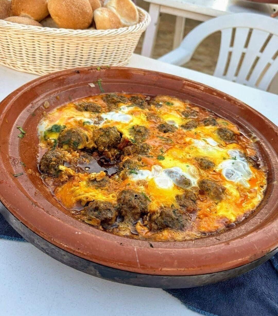 A clay dish with a meal, possibly a stew or casserole, on a table.