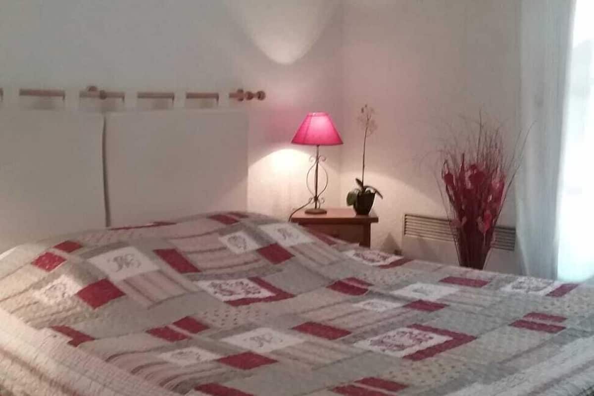 Ein Schlafzimmer mit einem großen Bett, einem Nachttisch mit Lampe, einer Topfpflanze und einem Wandradiator.