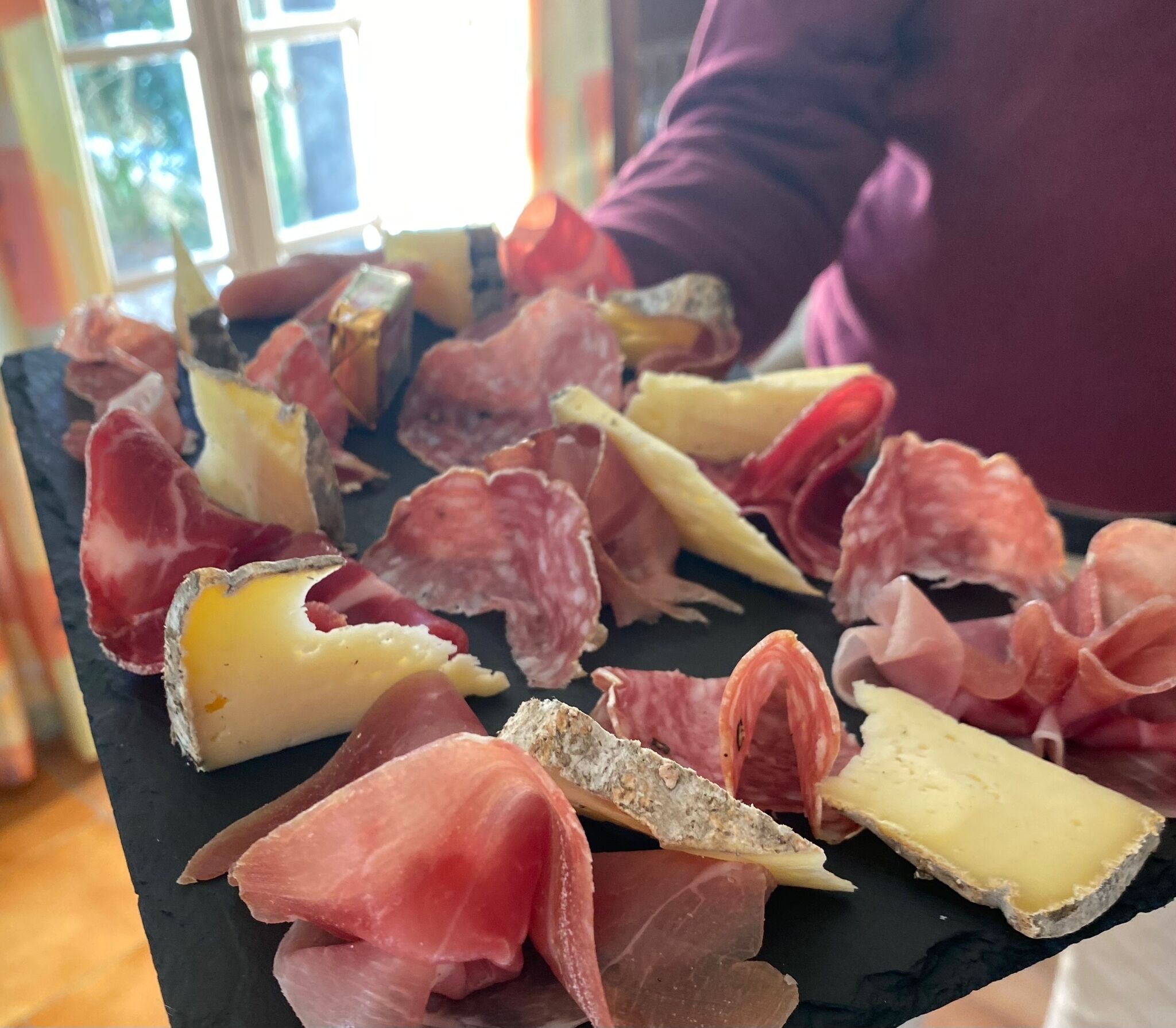 Une ardoise noire sur laquelle sont disposés divers types de charcuterie et de fromages.