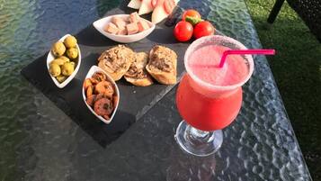 Una mesa con diferentes alimentos y bebidas, incluyendo una bebida azul, un refresco rojo con pajita, y varios cuencos con frutas y aperitivos.
