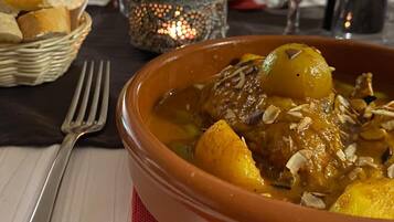 A dining table with a bowl of stew, a bottle of wine, and a basket of bread.