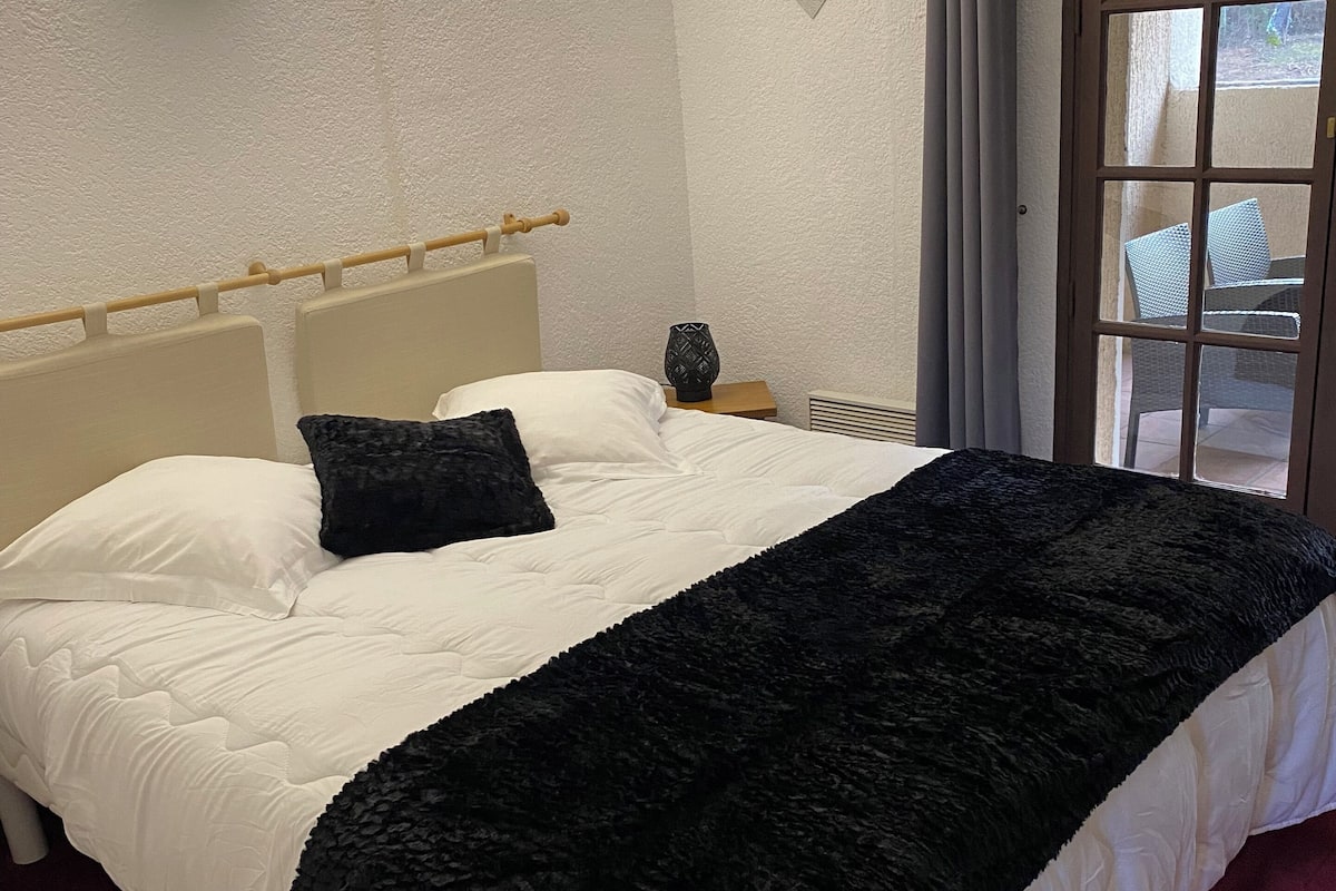 Ein Hotelzimmer mit einem Bett, einem Nachttisch, einer Lampe und Blick ins Freie durch ein Fenster.
