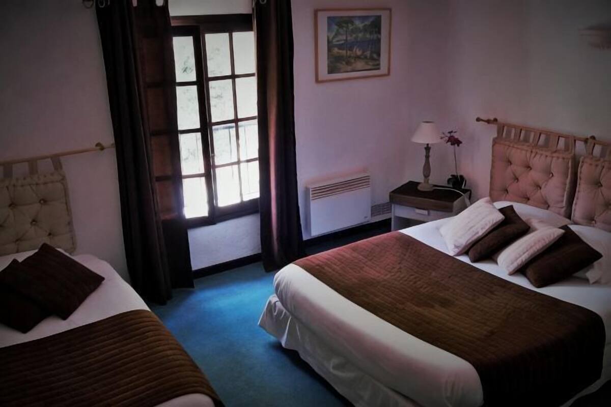 Ein Hotelzimmer mit zwei Betten, einem Fenster, einem Nachttisch, einer Lampe und einem Bild an der Wand.
