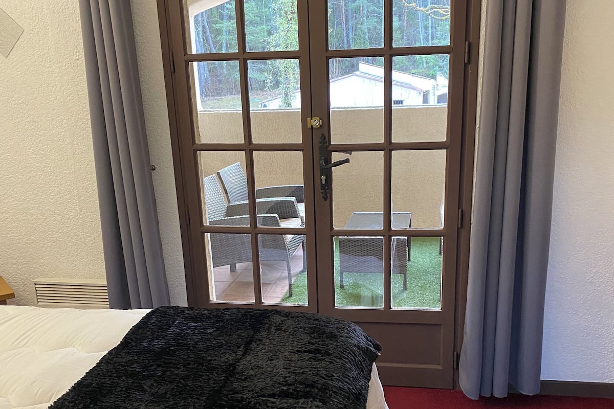 Ein Hotelzimmer mit Bett, einem Fenster mit Vorhängen und Blick auf Gartenmöbel.