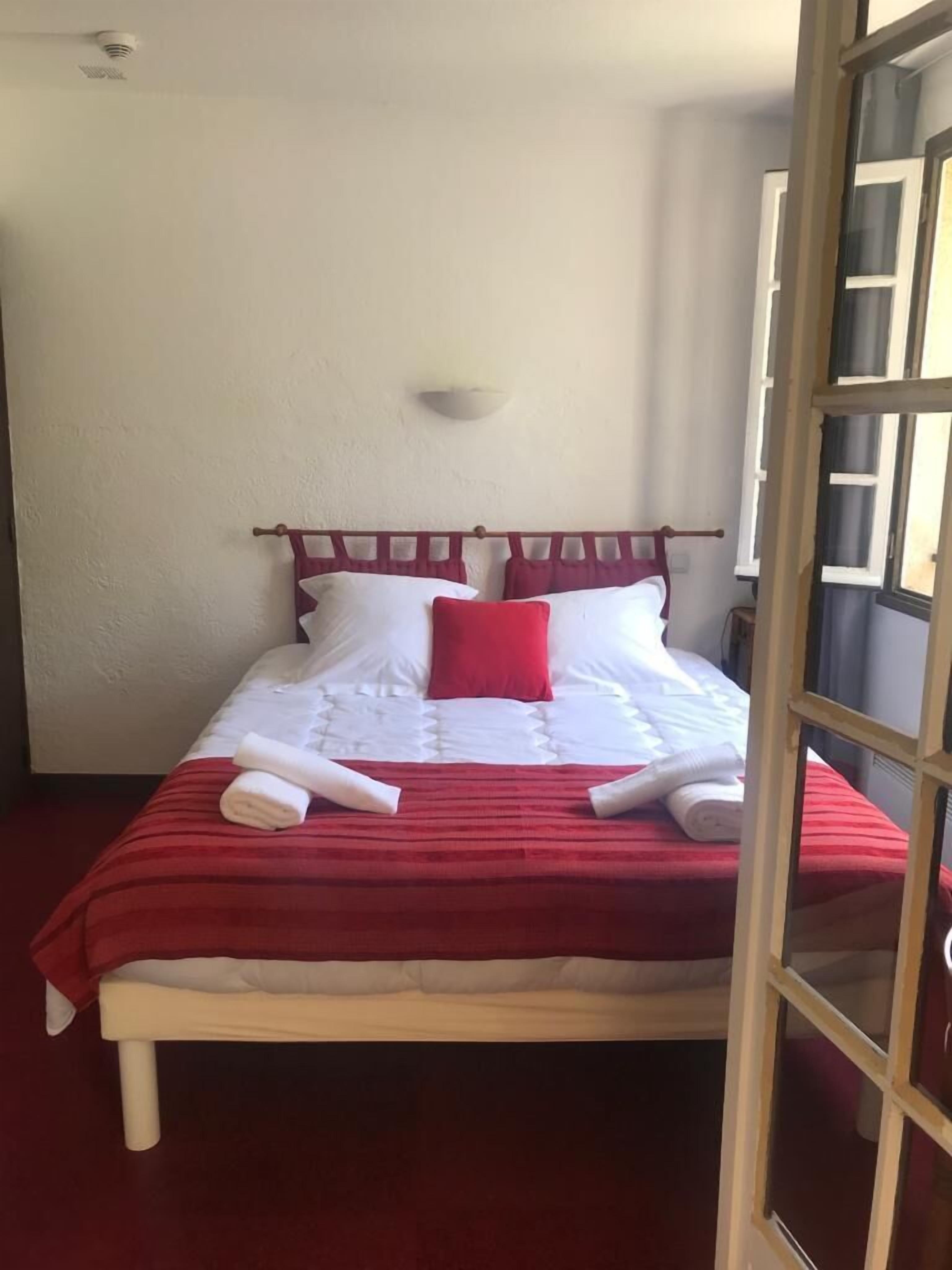 Un lit recouvert d’une couverture rouge et blanche, deux serviettes enroulées et un oreiller rouge.