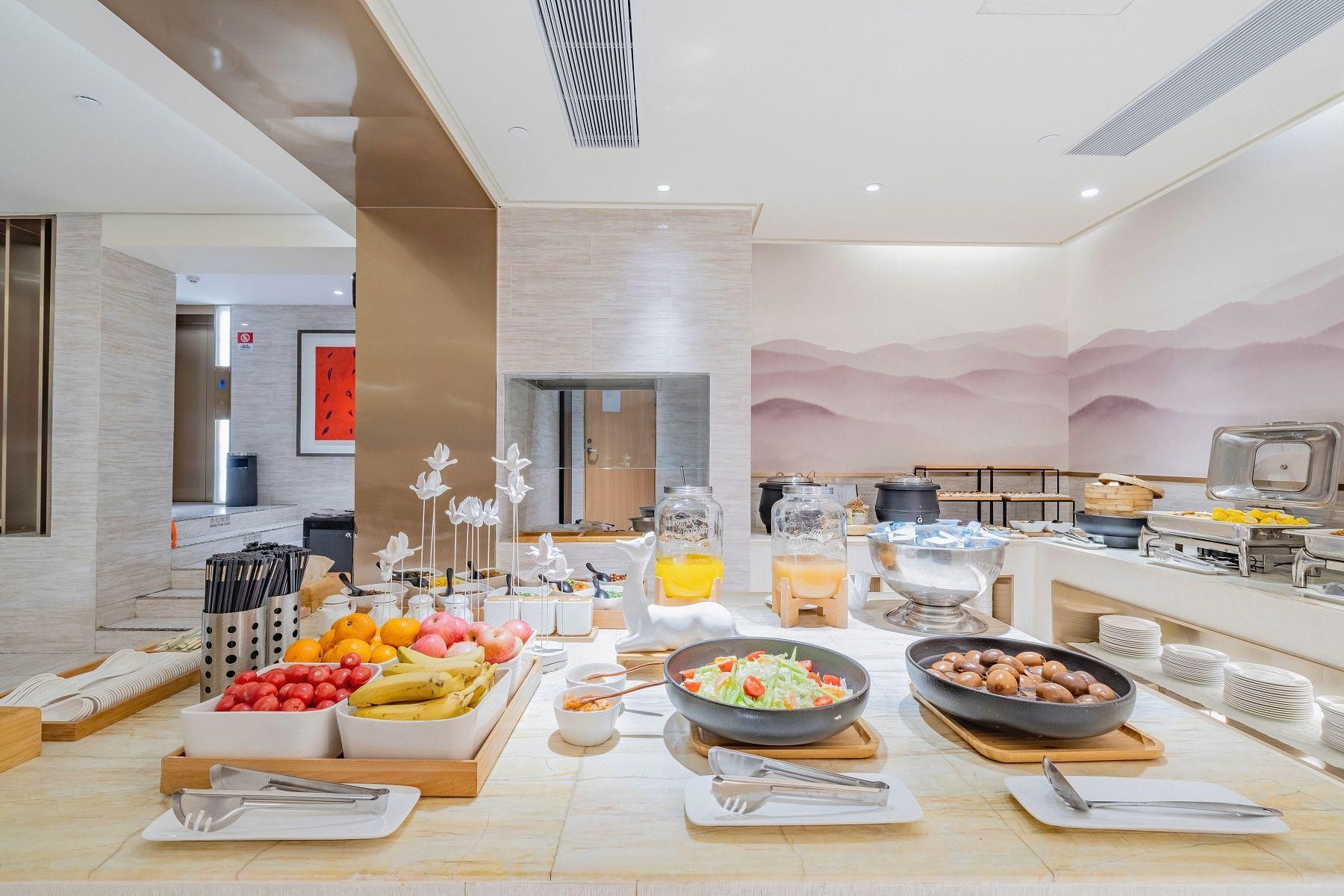 A buffet setup with various food items, utensils, and a kitchen area in the background.