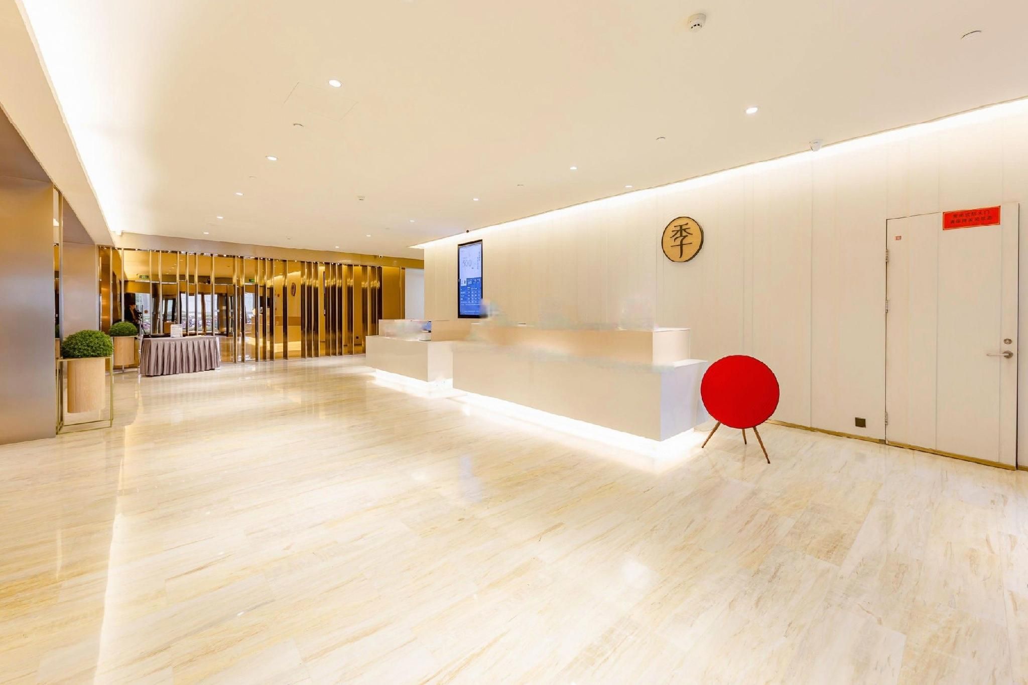 A modern hotel reception area with a marble floor, a reception desk, a digital screen, and a red chair.
