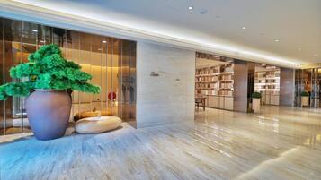 A modern lobby with a large potted plant, a marble floor, and a glass wall with a view of the interior.